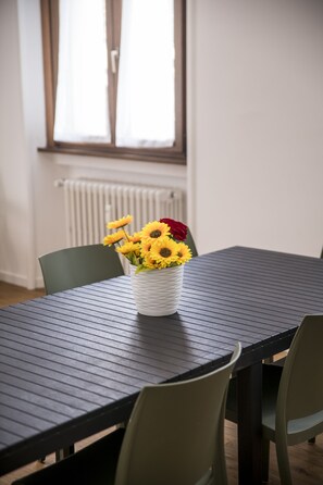 A dining table with a white vase containing sunflowers, two green chairs, and a window with blinds. - Hearth City Center Milan (MI)
