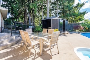 Une terrasse extérieure avec une table et des chaises à plateau en verre, un barbecue et une piscine.