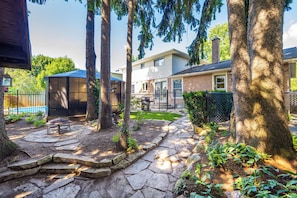 Un jardin avec une terrasse en pierre, un barbecue et une piscine.