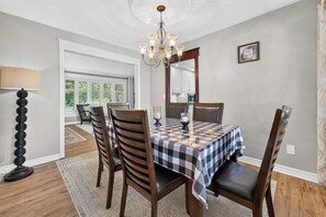 Un coin repas avec une nappe à carreaux, des chaises en bois, un lustre et une vue par la fenêtre.