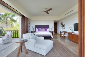 Une chambre spacieuse avec un grand lit, un ventilateur de plafond, un bureau et une vue sur les palmiers depuis le balcon.