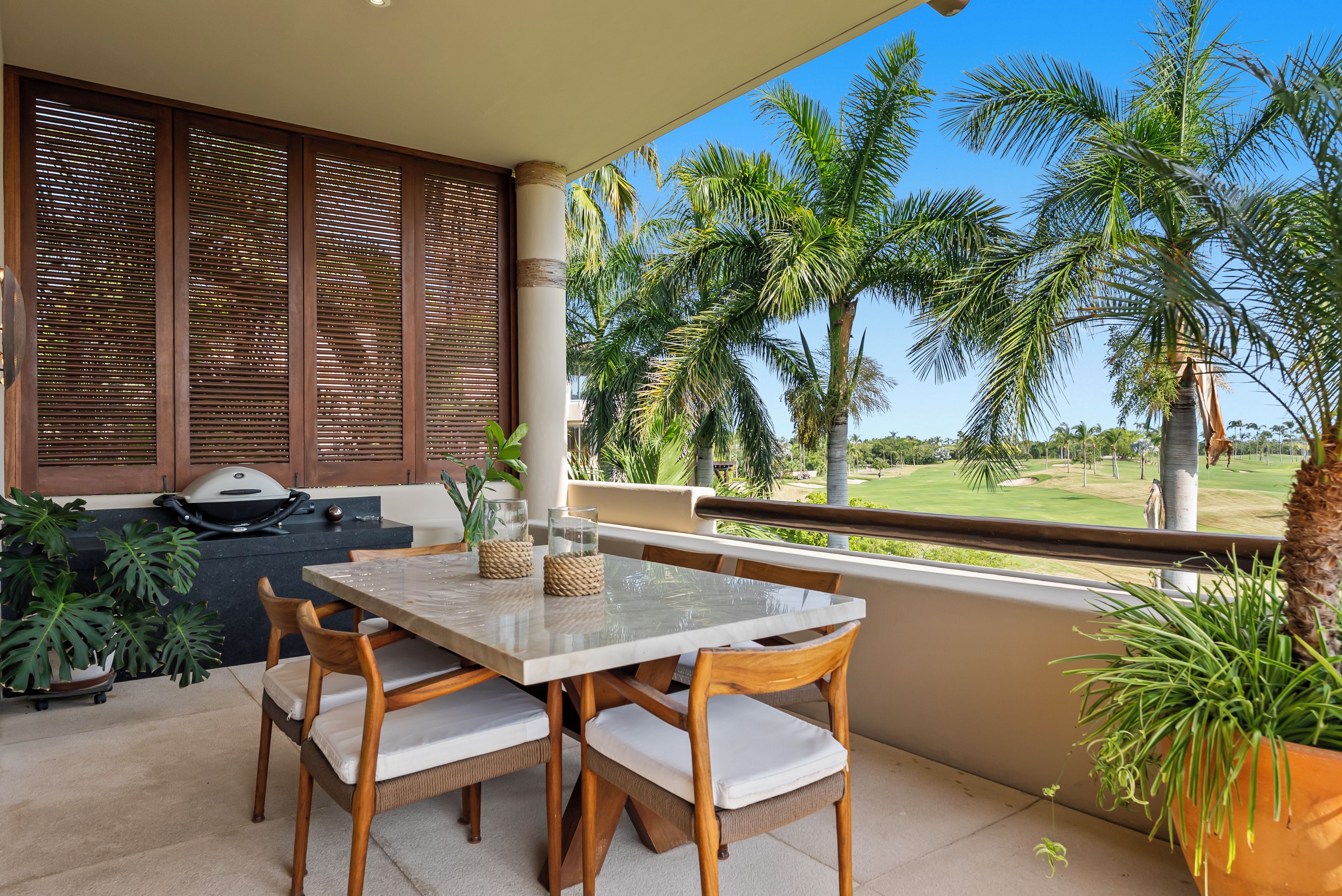 A balcony with a table and chairs, a grill, and a view of a golf course.