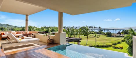 Ein moderner Poolbereich im Freien mit einer Holzterrasse, Liegestühlen und Blick auf das Meer und die Hügel.