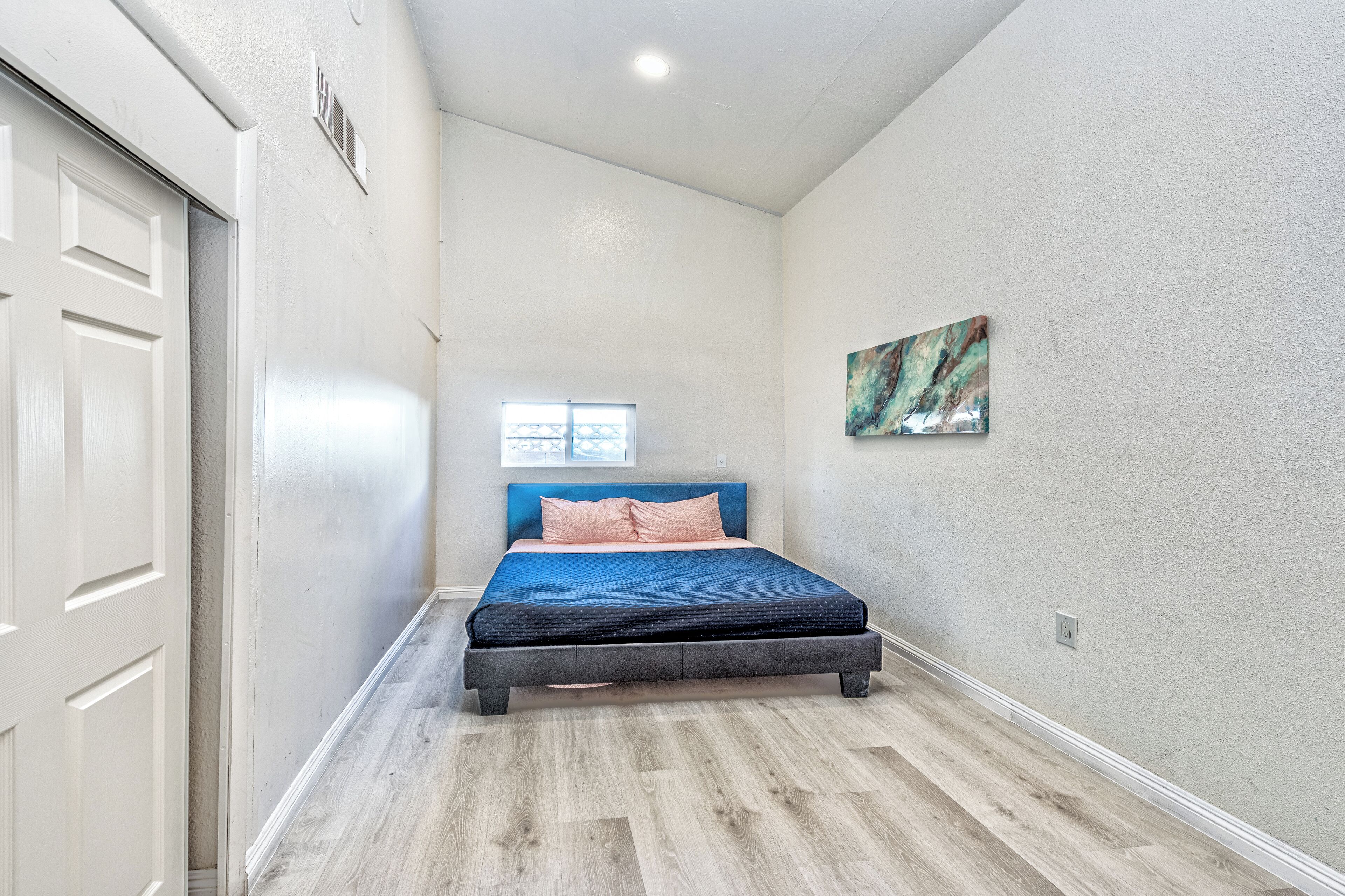 A bedroom with a bed, a window, and a painting on the wall.