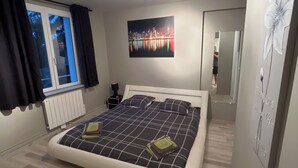 A bedroom with a bed, a window, a radiator, a painting, and a mirror. - -In Valjc- (Liverdun)