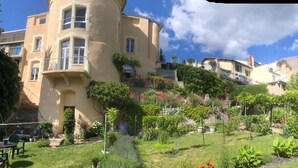 A multi-story building with balconies, a garden with various plants and flowers, and a clear sky. - -In Valjc- (Liverdun)