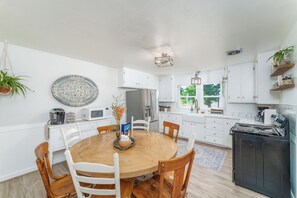 A modern kitchen with white cabinetry, a round wooden table, and a black stove. - Private Hot Tub, Large Fenced Yard, No Pet Fee (Colorado Springs)