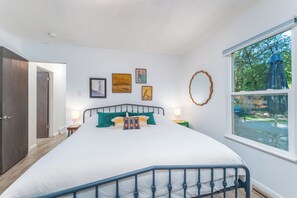 A bedroom with a large bed, a window with a view of the outdoors, and several framed artworks on the wall. - Private Hot Tub, Large Fenced Yard, No Pet Fee (Colorado Springs)