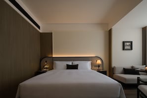 Een hotelkamer met een groot bed, nachtkastjes, een stoel en een aan de muur hangend schilderij.