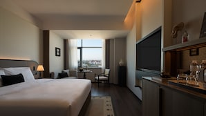 Een hotelkamer met een bed, een bureau, een stoel, een televisie en uitzicht op de stad.