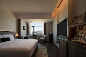 Een hotelkamer met een bed, een bureau, een stoel, een televisie en uitzicht op de stad.