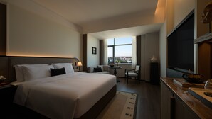 Een hotelkamer met een groot bed, een bureau, een stoel, een televisie en een raam met uitzicht op de stad.