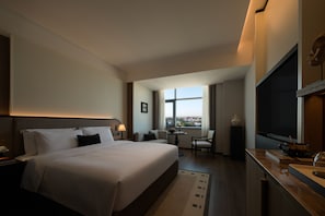 Een hotelkamer met een groot bed, een bureau, een stoel, een televisie en een raam met uitzicht op de stad.