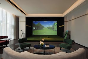 Een moderne kamer met een groot scherm waarop een golfspel wordt getoond, zithoek en een klein tafeltje met een vaas.