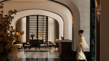 A hotel lobby with a geometric patterned floor, arched ceiling, and a seating area with a view through a grid-like window.