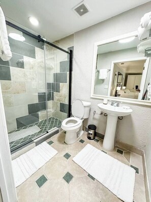 Ein Badezimmer mit Duschkabine aus Glas, Toilette, Waschbecken und Spiegel.