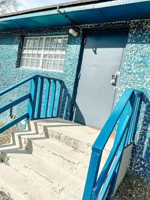 Eine Treppe mit blauen Geländern führt zu einer Tür mit einem Fenster darüber.