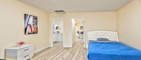 A bedroom with a bed, a bedside table, a chair, a desk, and a bathroom visible through an open door.