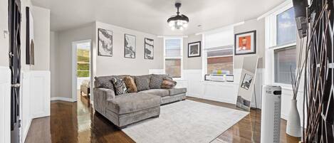A modern living room with a grey sectional sofa, a large white rug, and a ceiling fan.