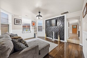 A modern living room with a grey sofa, a flat-screen TV mounted on a hexagonal wall, and a ceiling fan. - Your Parkside Executive Retreat + Dedicated Office (Chicago)
