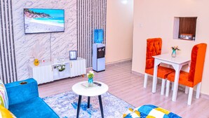 Un salon moderne comprenant un canapé, une table basse, un téléviseur fixé au mur et un coin repas avec des chaises et une table.