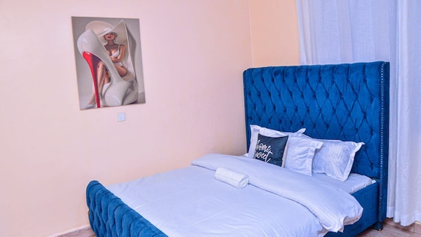 Une chambre à coucher comprenant un lit, une tête de lit, un oreiller, une couverture, un tableau accroché au mur et un rideau.