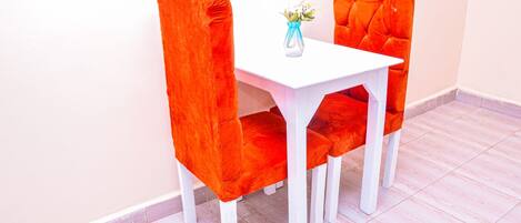 A dining table with two chairs, a vase with flowers, and a white wall.
