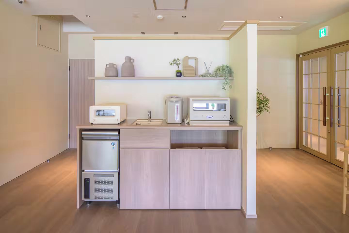 A kitchenette with a refrigerator, microwave, and toaster, a wooden cabinet, and a shelf with decorative items.