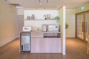 A kitchenette with a refrigerator, microwave, and toaster, a wooden cabinet, and a shelf with decorative items.