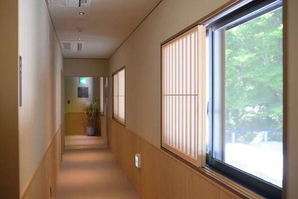 A corridor with a wooden floor, a potted plant, and a window with blinds.