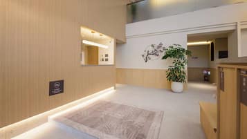 A modern hotel lobby with a reception desk, a large potted plant, and a wall-mounted mirror.
