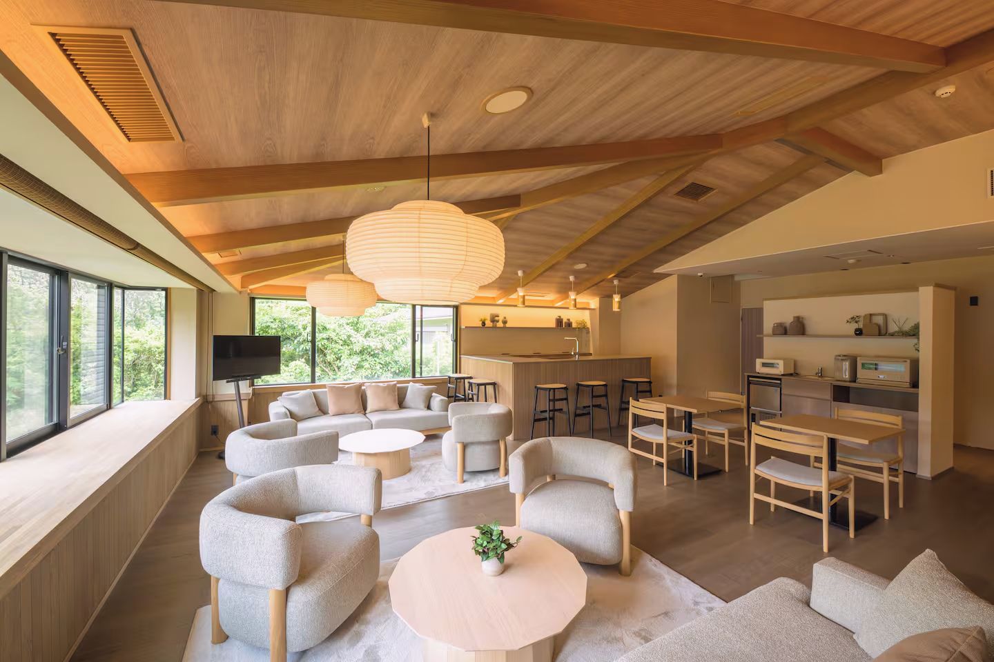 A modern interior with a living area, kitchen, and dining space, featuring wooden beams, large windows, and contemporary furniture.