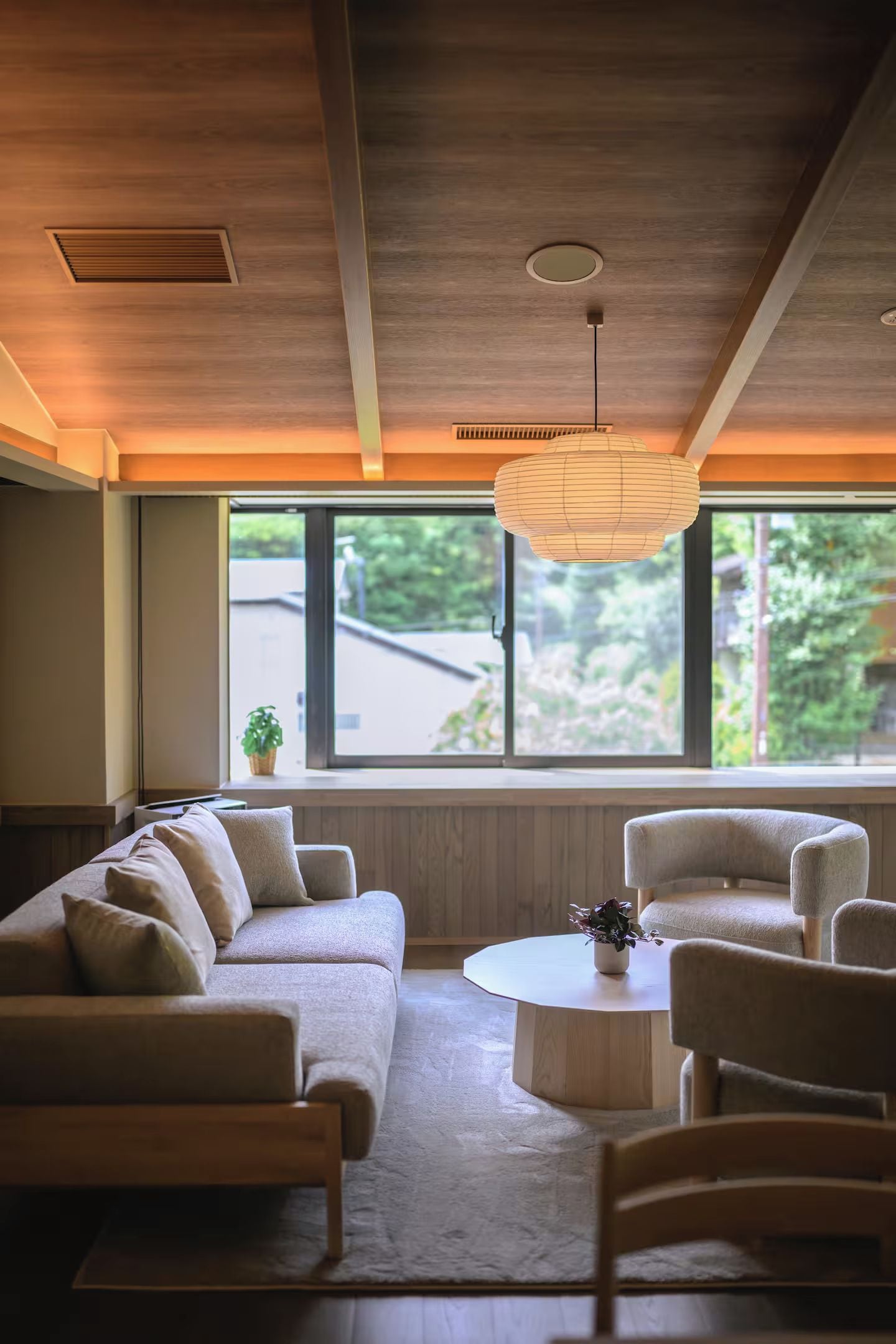 A modern living room with a sofa, chairs, a coffee table, and a large window with a view of greenery.