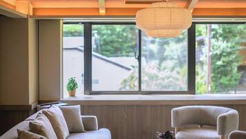 A modern living room with a sofa, chairs, a coffee table, and a large window with a view of greenery.