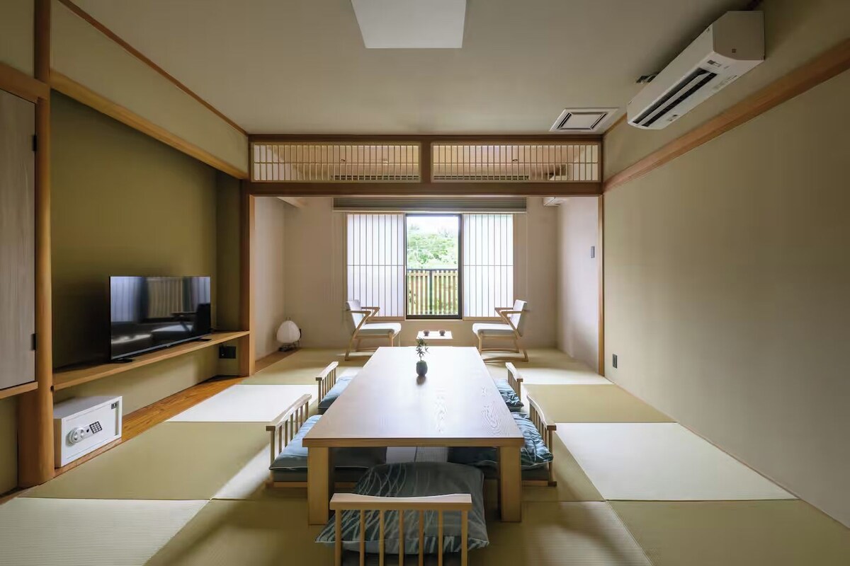 Quarto em estilo japonês tradicional com tatames, uma mesa baixa e uma televisão em uma prateleira.
