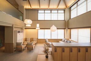 A modern hotel lobby with a seating area, a reception desk, and a large window with vertical blinds.