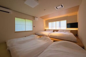 Ein Hotelzimmer mit zwei Betten, einem Wand-Fernseher und einem Fenster mit vertikalen Jalousien.