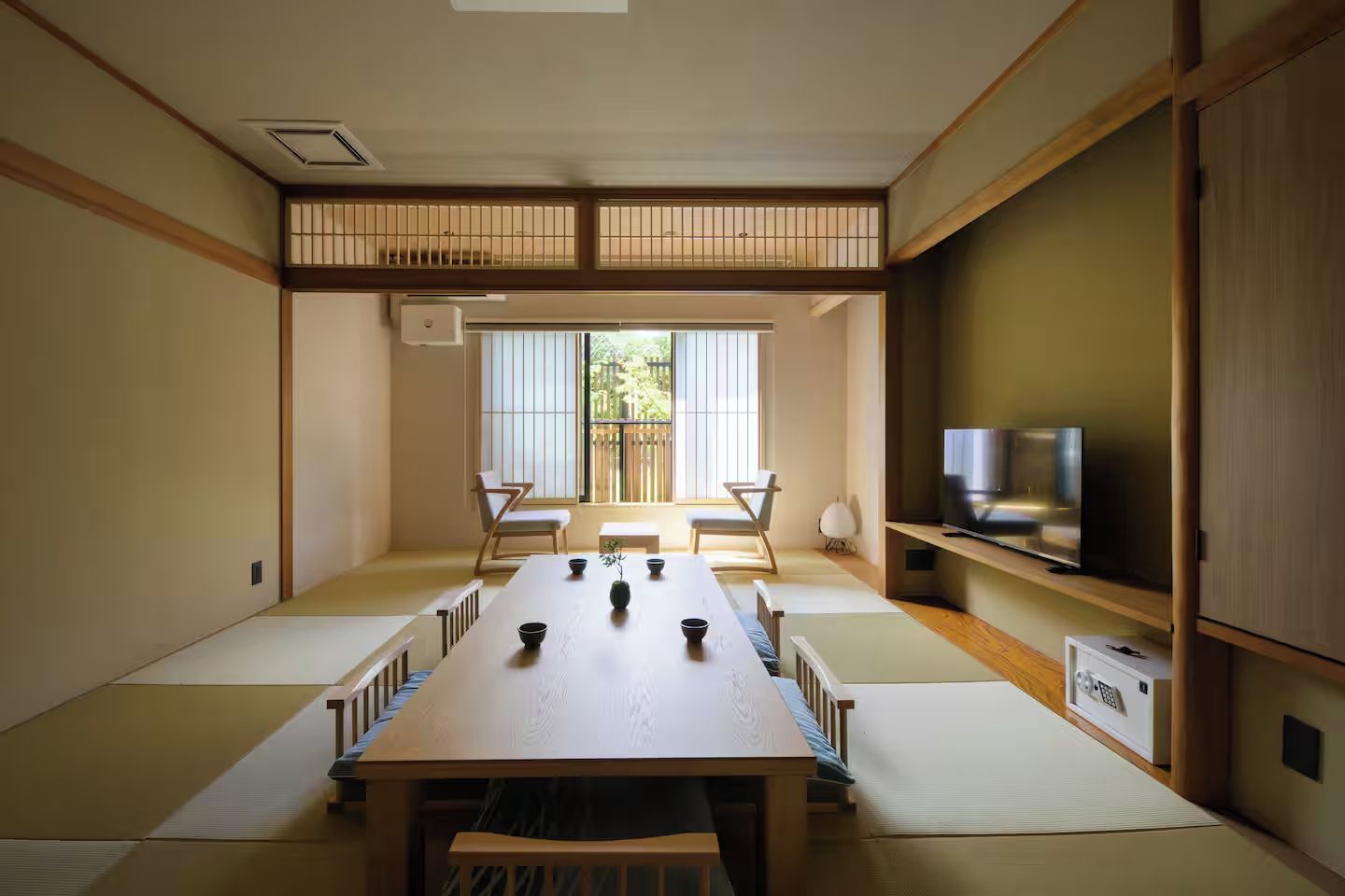 Perinteinen japanilaistyylinen huone, jossa on tatamimatto, matala pöytä tyynyineen ja televisio puuhyllyllä.
