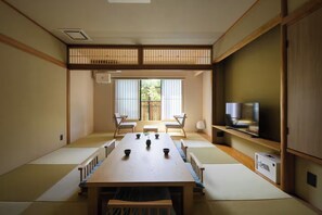 Habitació japonesa tradicional amb fons de paret de tatami, una taula baixa amb coixins i una televisió sobre una estant de fusta.