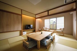 Ein traditioneller japanischer Raum mit Tatami-Bodenbelag, einem niedrigen Holztisch und einem Fernseher auf einem Regal.