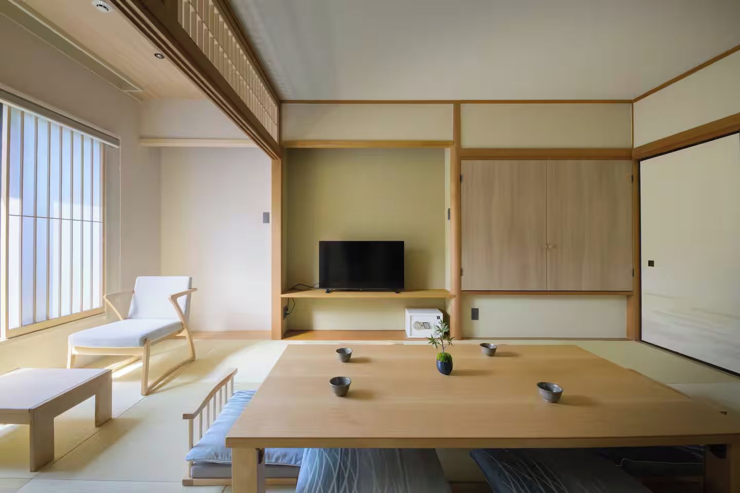 A traditional Japanese-style room with tatami flooring, a low table, a television on a shelf, and a sliding door.