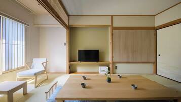 A traditional Japanese-style room with tatami flooring, a low table, a television on a shelf, and a sliding door.