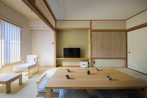 Et traditionelt japansk værelse med tatami-gulv, et lavt bord, et fjernsyn på en hylde og en skydedør.