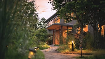 A modern house with a pathway leading to the entrance, surrounded by lush greenery.