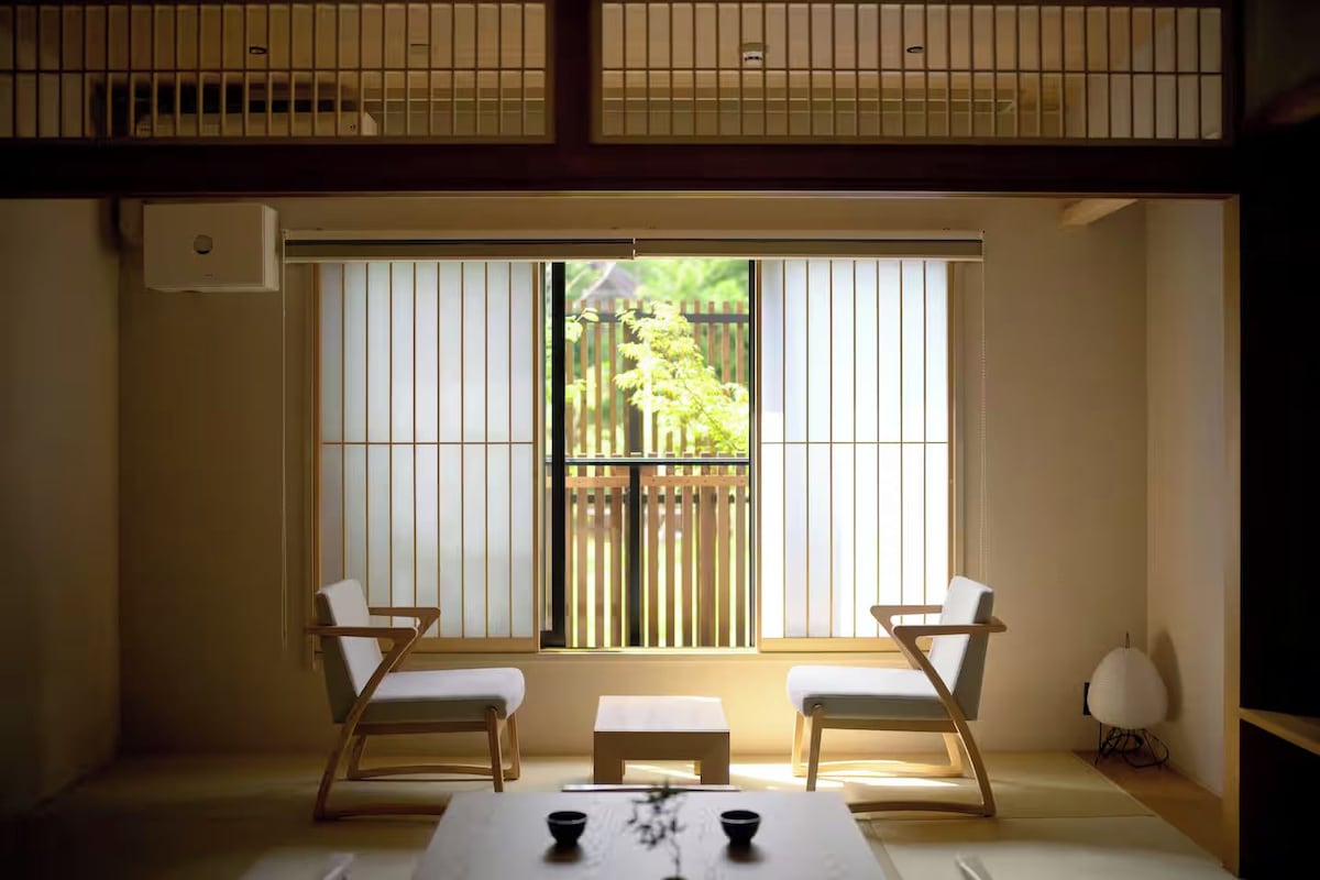 Quarto com um painel deslizante shoji, duas cadeiras, uma pequena mesa e um abajur tradicional japonês.