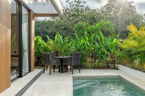 Eine moderne Außenpatio mit Pool, umgeben von üppiger Vegetation und einem Essbereich mit Stühlen und Tisch.