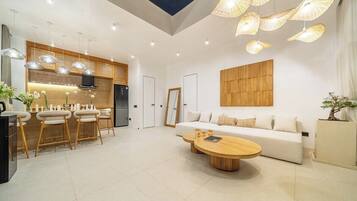 A modern kitchen with pendant lighting, a dining area with stools, a sofa, and a coffee table.