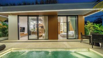 A modern house with a swimming pool, large glass doors leading to a living area, and a dining area.