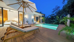 Una casa moderna con piscina, terraza de madera y sillones de descanso.