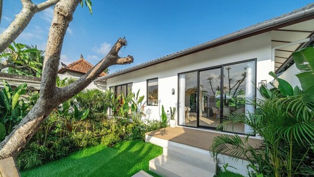 Una casa moderna con un patio, abundante vegetación y cielo despejado.